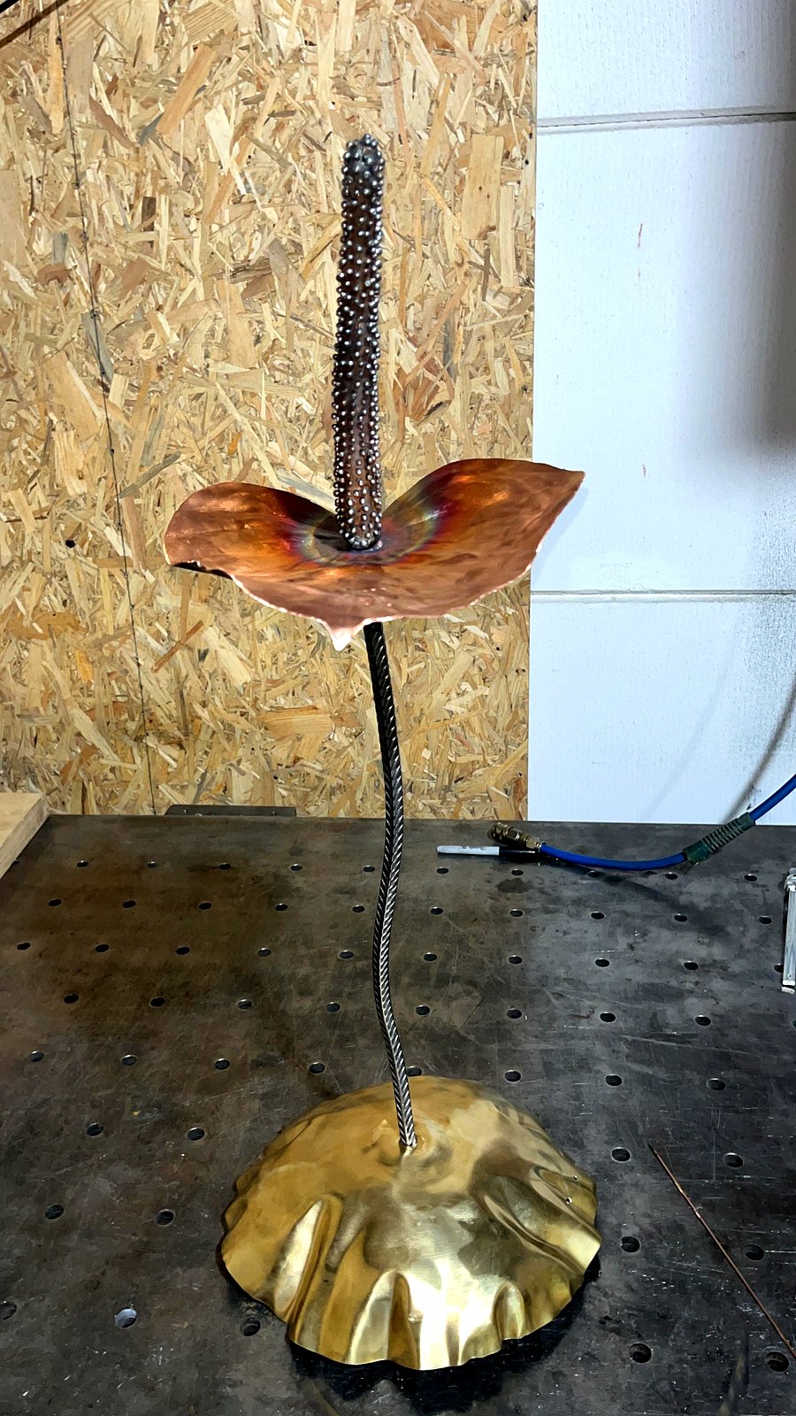 Compleet, gesigneerd op de voet van messing — ooit een drumbekken. Een anthurium die altijd bloeit.
